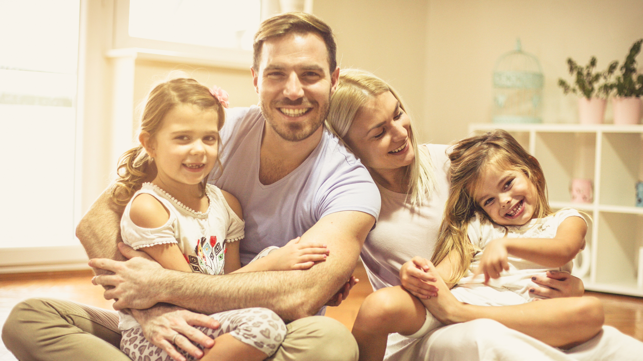 An image of a young family of four at home, portraying a warm and inviting living room scene. The parents are engaged with their two children, creating a joyful and harmonious family atmosphere.